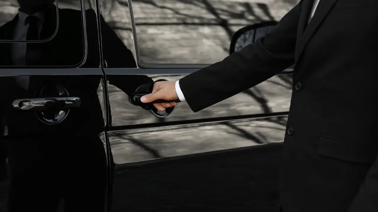 chofer de terno abrindo a porta de um carro de luxo